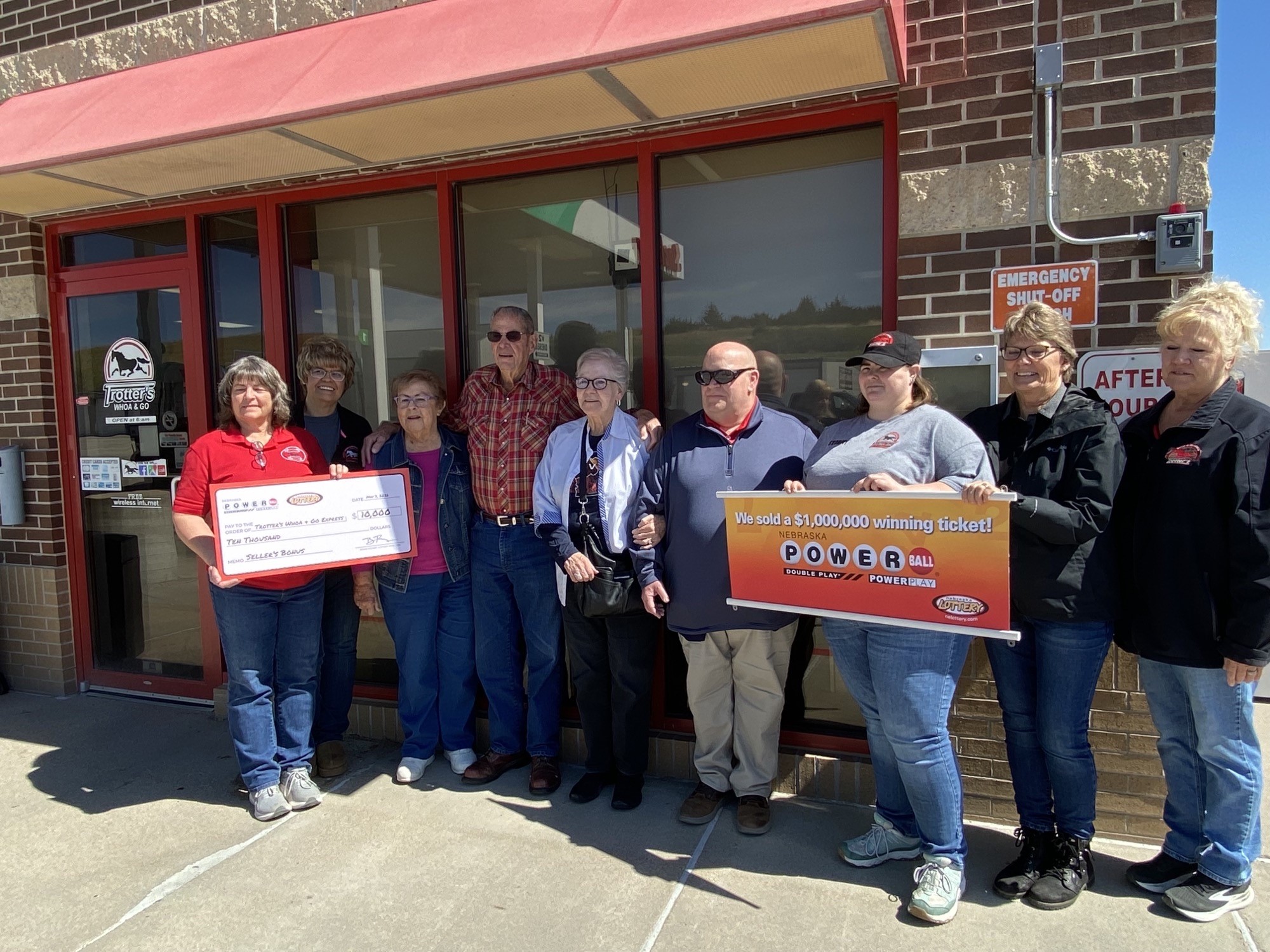 A group of store employees stand outside Trotter's Whoa & Go in Ord. One person holds a large novelty check for $10,000. Another holds a sign that reads, "We sold a $1,000,000 winning ticket!"
