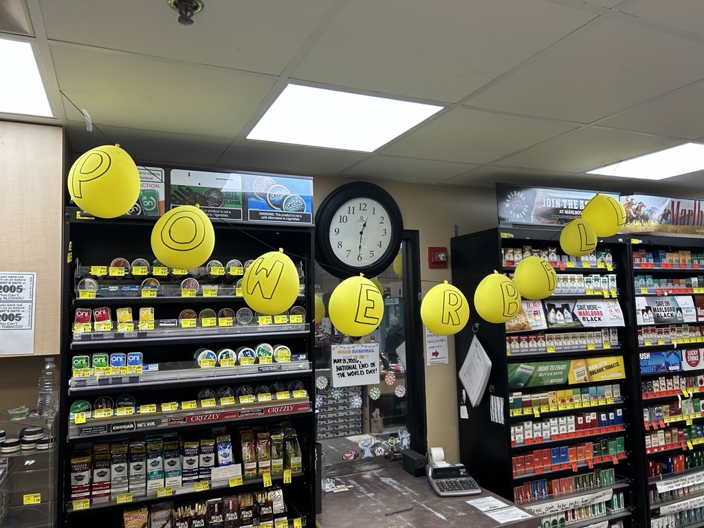 Shot of Russ's Market customer service. A banner of yellow ballons is hanging from the ceilling spelling out the word POWERBALL.